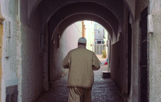 A man in traditional attire walks through a picturesque Moroccan alley.