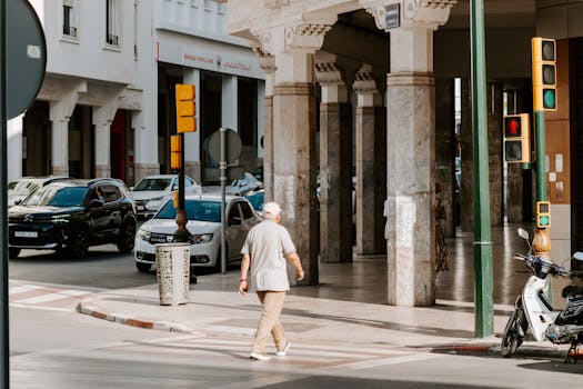 Older man in a cap crossing a sunny street beside colonnaded buildings in Rabat