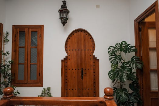 Porte en bois en arc outrepassé à côté d'une fenêtre en bois, avec une lanterne suspendue et des plantes vertes