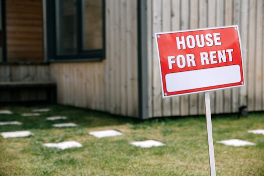 A modern wooden house with a prominent 'House for Rent' sign in the green yard.