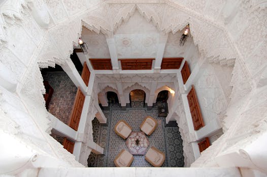 View looking down into the courtyard of a traditional Moroccan riad, with carved white arches, zellige tiles and seating around a central table