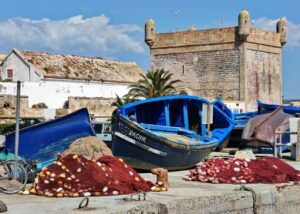 Colorful fishing boats and nets by the historic fort in Essaouira, Morocco, under a clear blue sky.