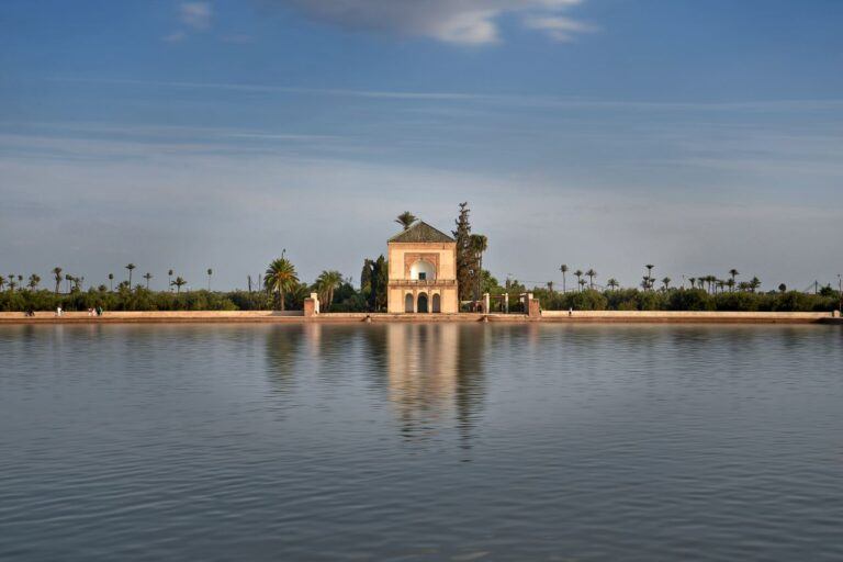 Tranquil view of Menara Gardens pavilion reflecting in water under a clear blue sky in Marrakech.