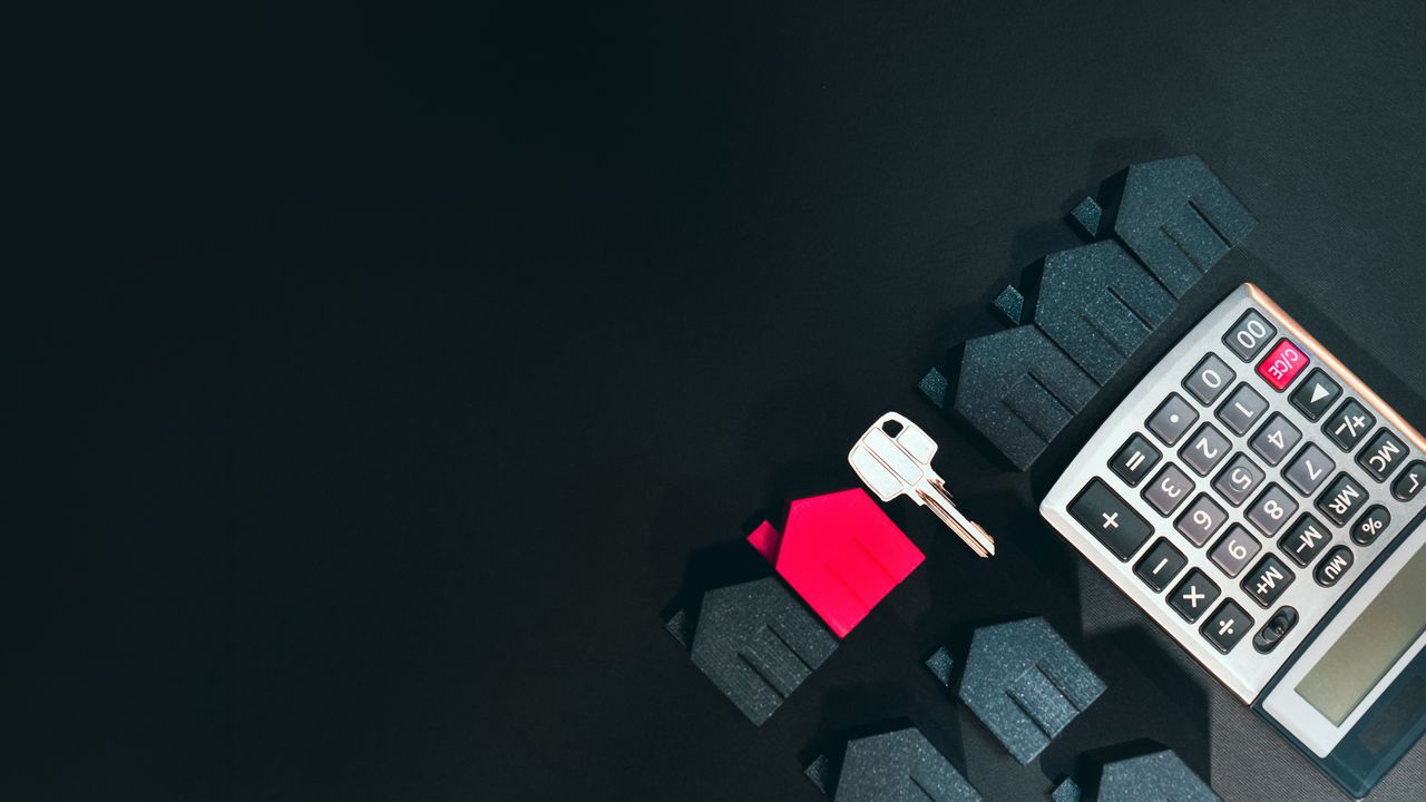 Real estate concept image featuring a calculator, houses, and a key on a black background.