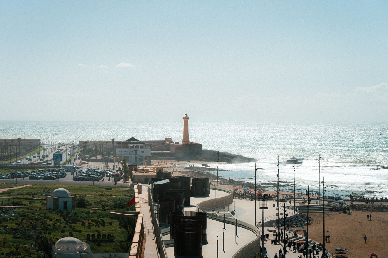 Moroccan coastal city with a lighthouse, a harbour wall, the ocean and a seafront promenade below