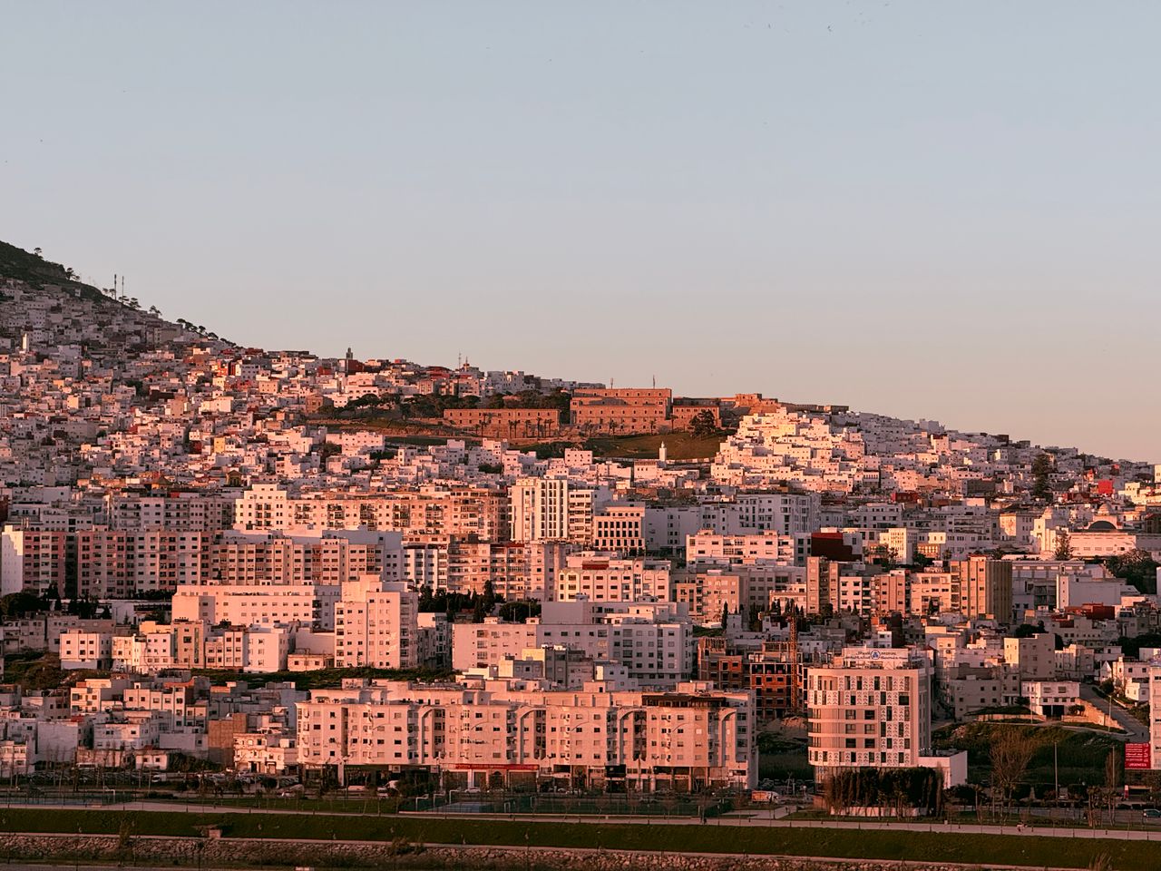 Immeubles blancs d'une ville marocaine étagés sur une colline, éclairés par le soleil couchant